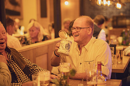 Gast hält lachend einen bayerischen Bierkrug im Maximilians Berlin